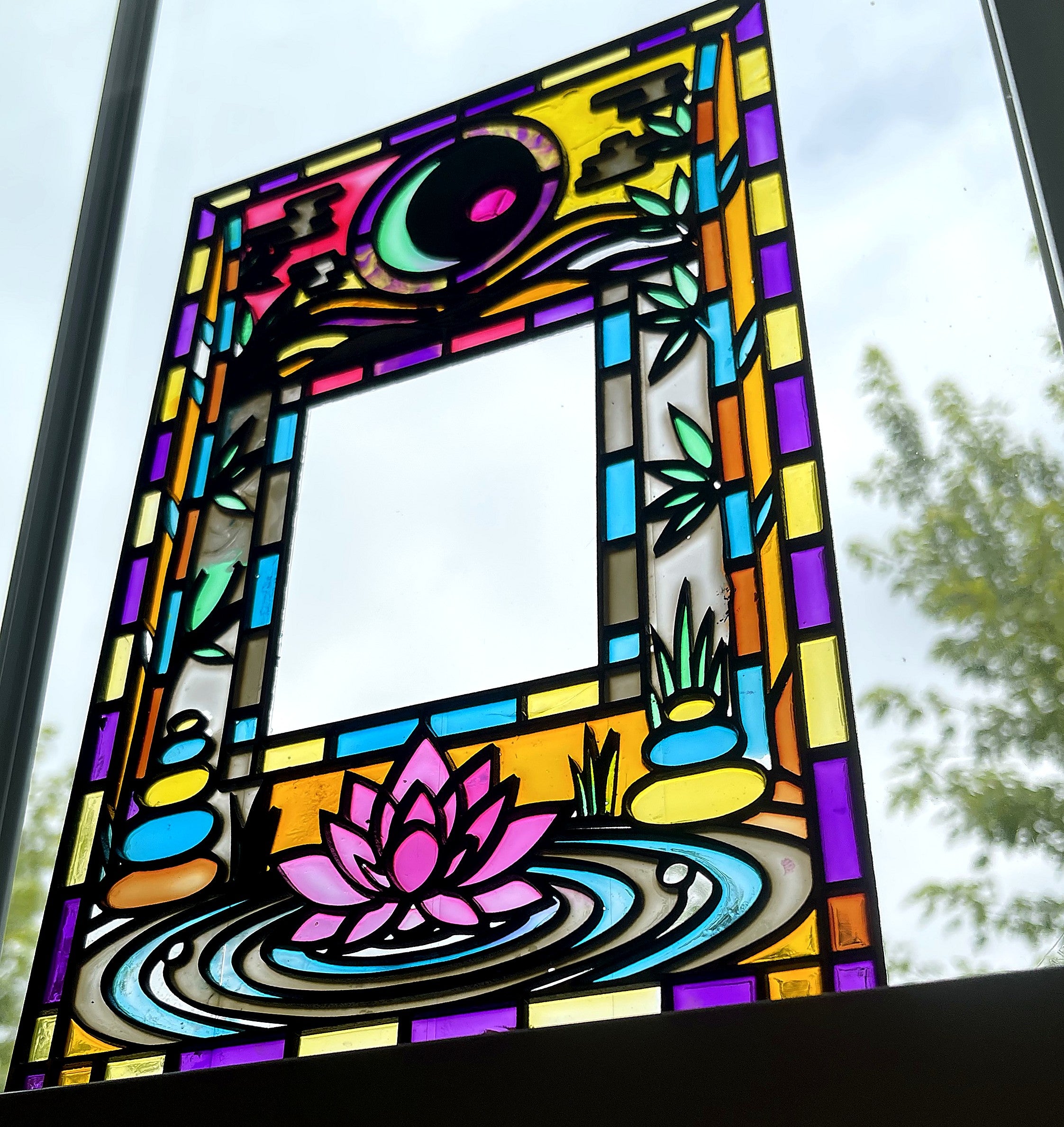 Lotus and moon stained glass style suncatcher panel hanging in a window, pink lotus on rippling water, crescent moon and cloud above, green bamboo down both sides